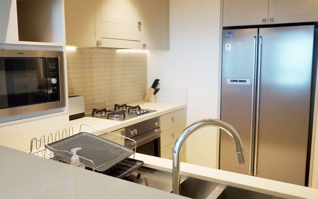 Modern apartment kitchen with white cabinetry, stone benchtops, and integrated appliances.